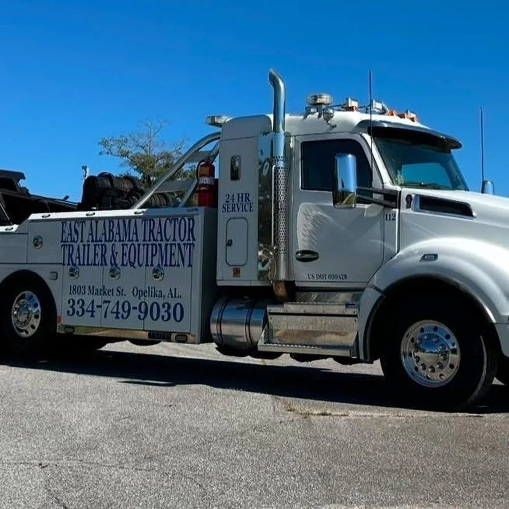 White Alabama Tractor Trailer & Equipment tow truck parked on a street under a clear blue sky.