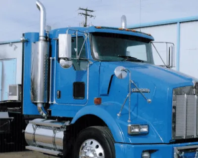 Blue Kenworth semi truck cab with a chrome exhaust stack parked beside a metal building