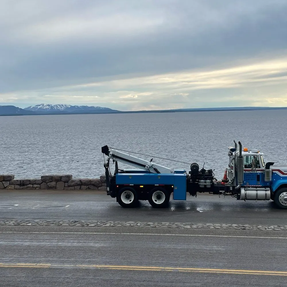 Blue heavy-duty wrecker towing a semi truck along a waterfront road