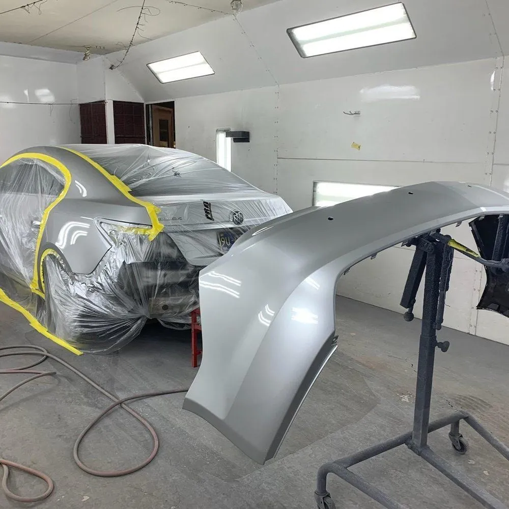 Paint booth with a plastic-masked silver car and a painted body panel on a stand