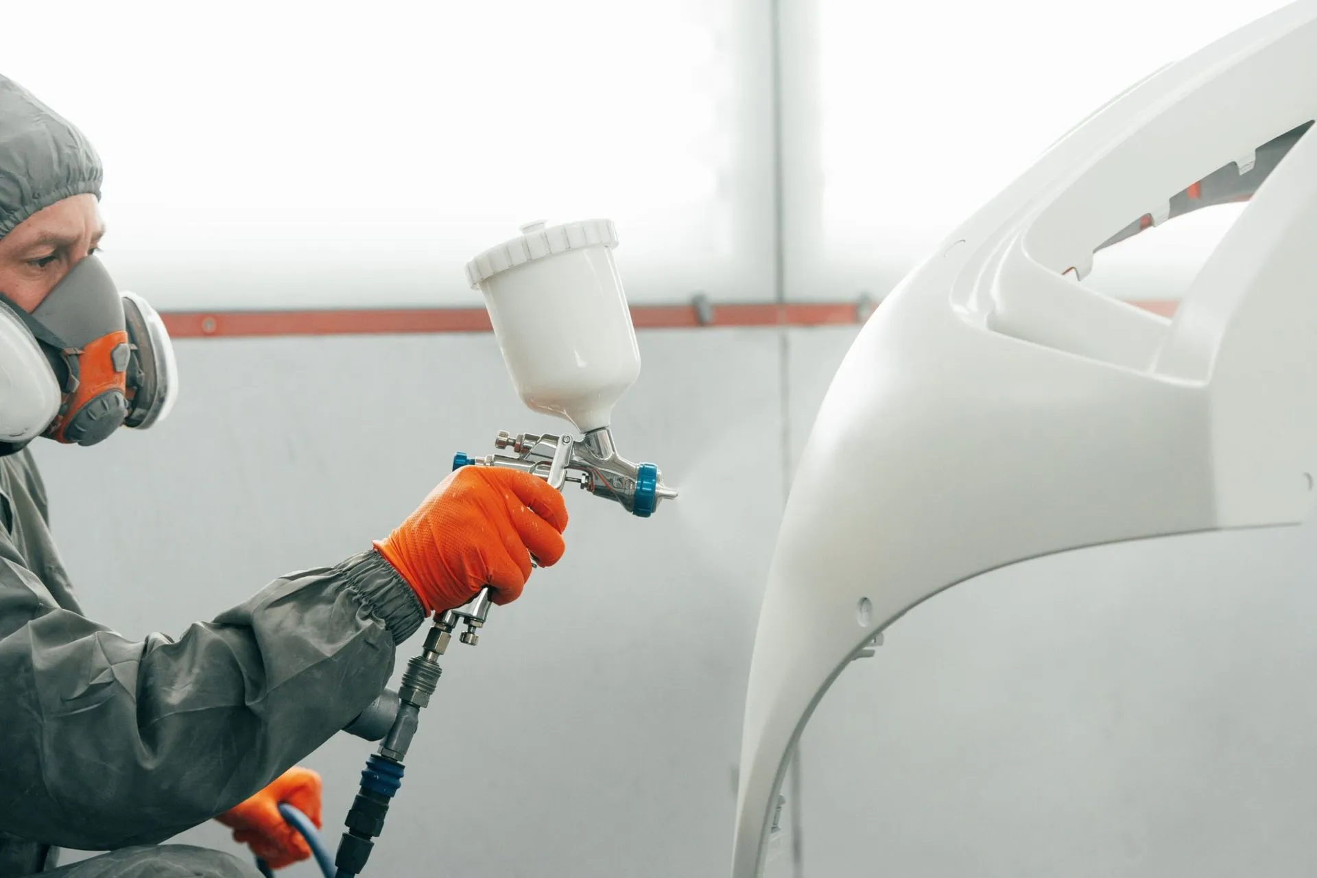 Painter in a respirator spraying a white body panel with a spray gun