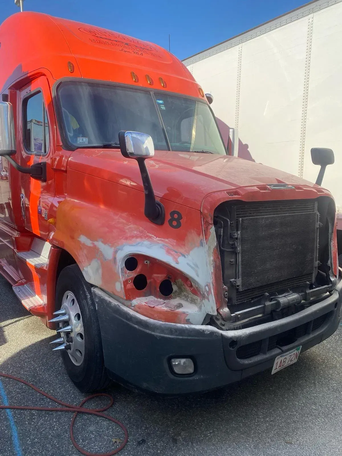 Orange semi truck with primer patches on its fiberglass hood and bumper during repair